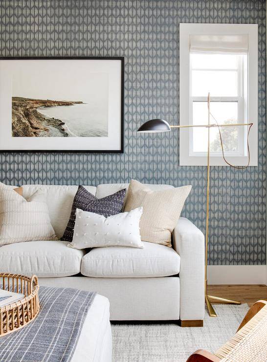 Living room features a white modern couch with tan accent pillows on a gray jute rug illuminated by a brass floor lamp and blue gray wallpaper.