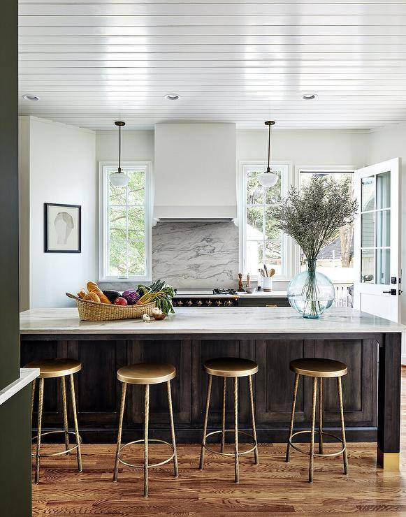 Kitchen features a brown island with a honed marble countertop and gold stools.