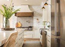Kitchen features a rustic French range hood on gray herringbone tiles, a white stone kitchen backsplash and a white kitchen island.