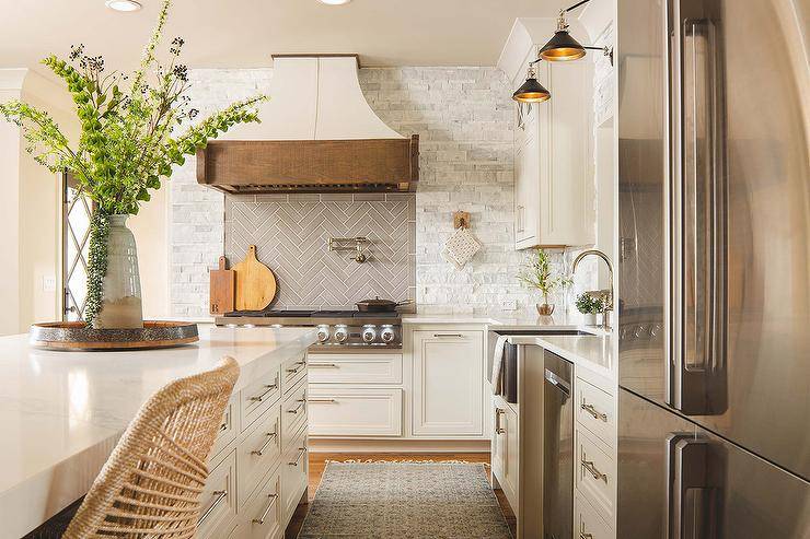 Kitchen features a rustic French range hood on gray herringbone tiles, a white stone kitchen backsplash and a white kitchen island.