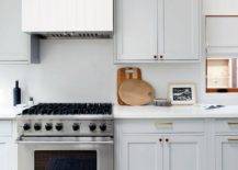 Kitchen features a white plank range hood mounted on white quartz slab kitchen backsplash over a stainless steel Viking range flanked by pale gray cabinets.