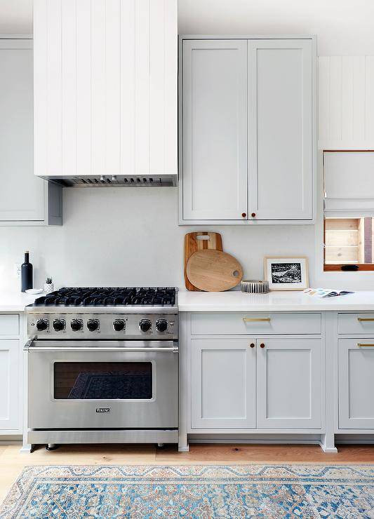 Kitchen features a white plank range hood mounted on white quartz slab kitchen backsplash over a stainless steel Viking range flanked by pale gray cabinets.