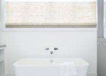 A chrome tub filler is mounted beneath a window and over a rectangular freestanding bathtub placed on white and gray marble hexagon floor tiles.