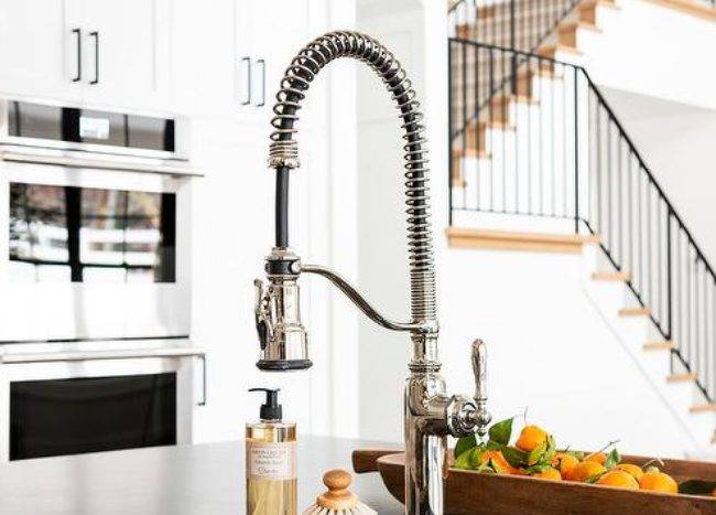 A black leathered granite kitchen countertop is fitted with a stainless steel sink matched with a stainless steel industrial pull-out faucet.