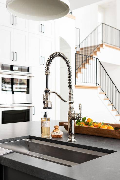 A black leathered granite kitchen countertop with stainless steel sink and industrial pull-out faucet.