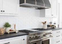 A stainless steel dual range is paired with a white brick backsplash and a silver and black hood.