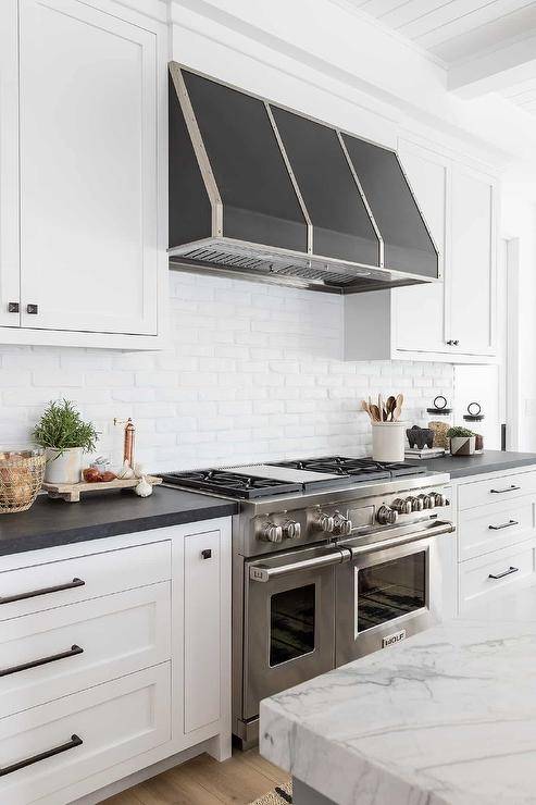 A stainless steel dual range is paired with a white brick backsplash and a silver and black hood.