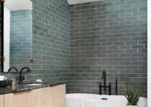 Green tiled bathroom walls complement a white oval freestanding bathtub paired with a matte black tub filler.