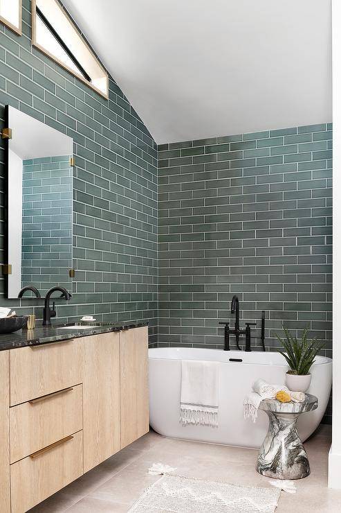 Green tiled bathroom walls complement a white oval freestanding bathtub paired with a matte black tub filler.