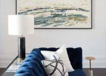 Living room features a blue velvet tufted couch with white pillows and a sofa table lit by black lamp.