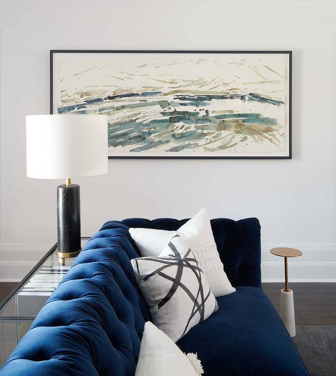 Living room features a blue velvet tufted couch with white pillows and a sofa table lit by black lamp.