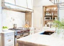 Kitchen features Darlana lanterns over a gray center island, a microwave cabinet with folding doors and a stove alcove with a white French range hood with stainless steel straps over a nickel swing arm pot filler and a Wolf dual range.