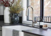 Farm sink and steel gray cabinets in a cottage kitchen designed with a brushed nickel gooseneck faucet and black leather granite countertops.