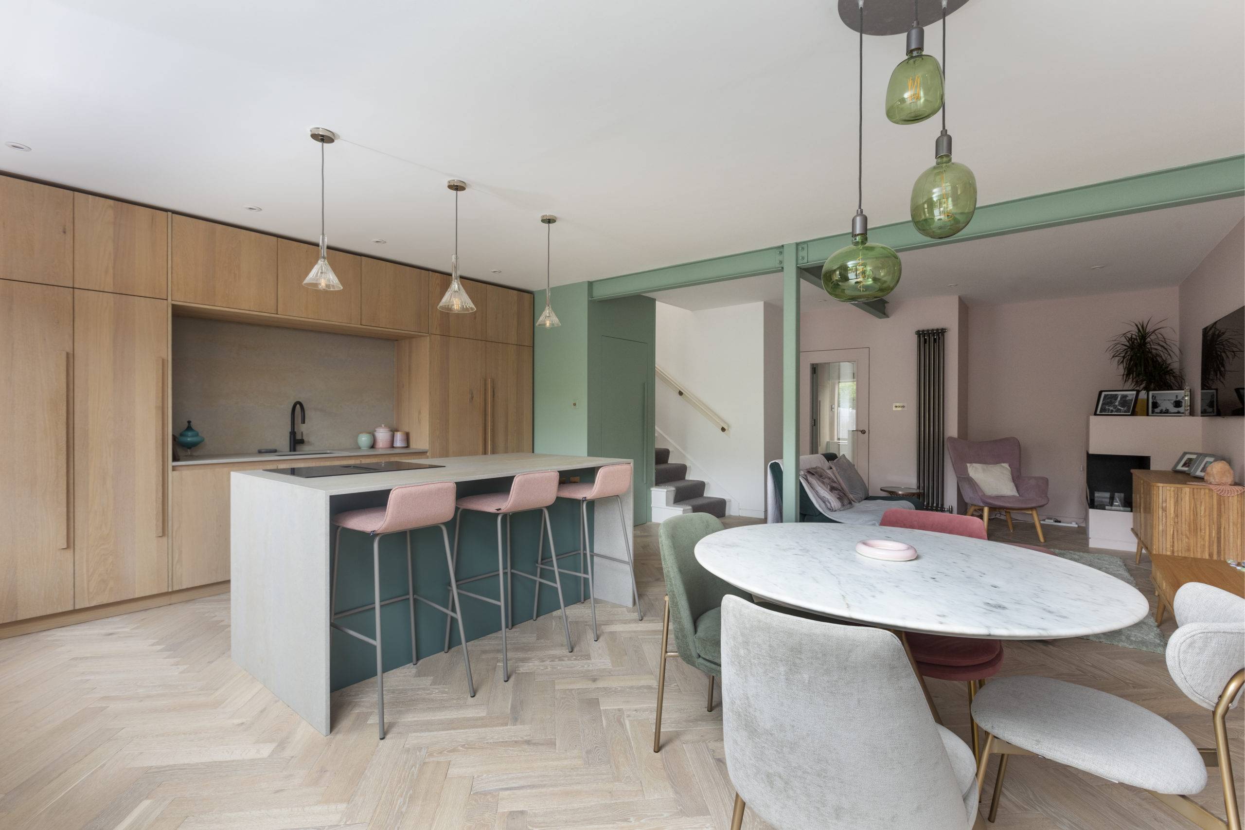 midcentury style open concept kitchen dining room living room with minimal furnishings, oak herringbone floor and pink & green color palette