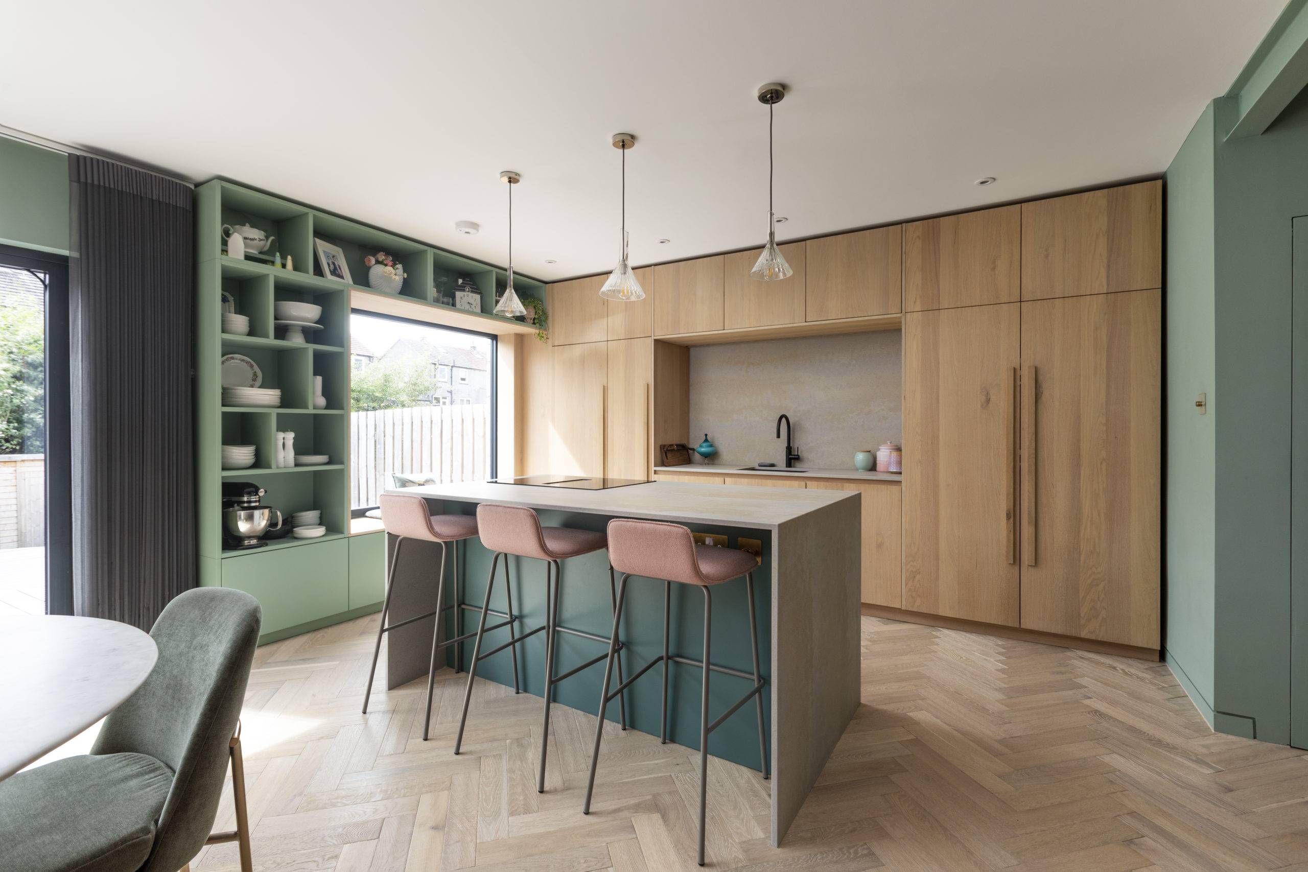 midcentury kitchen with pink barstools at stone island and light wood cabinetry