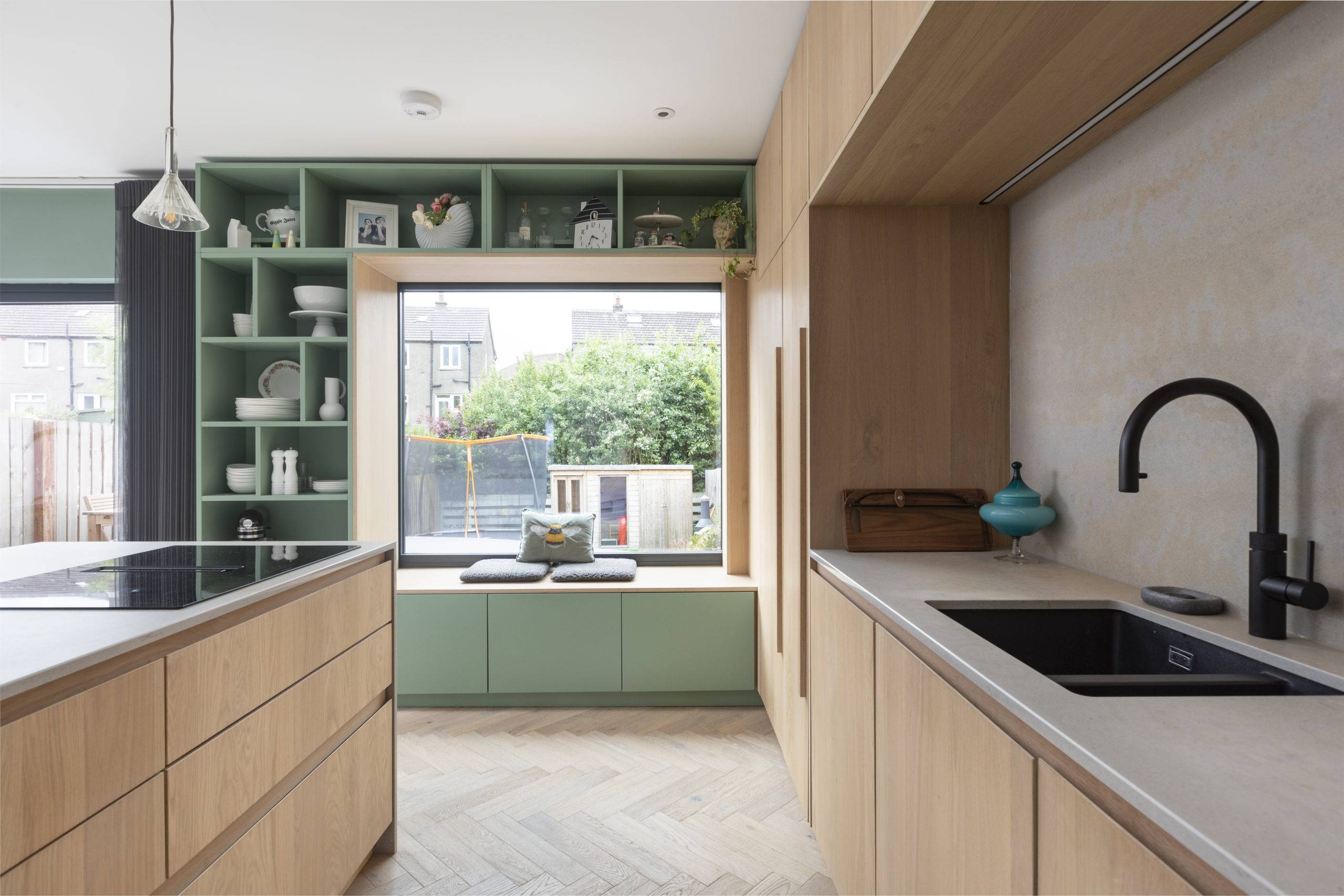 green custom shelving built in around large window seat in kitchen with large oak doors and black sink in alcove