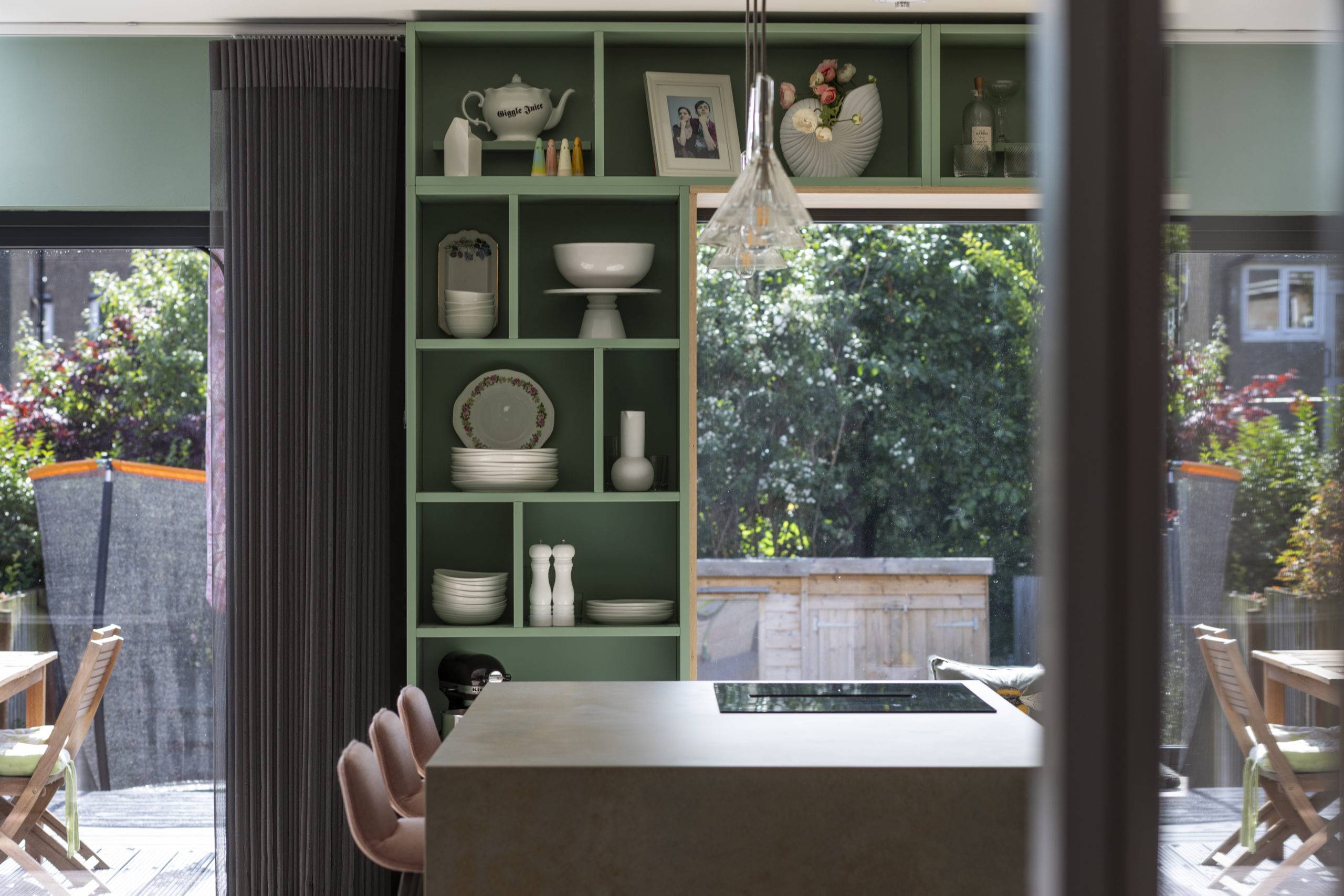 custom green floor to ceiling shelving display plates, vases, and belongings around large window seat