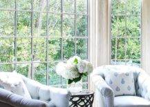 A pair of two pale blue tufted chairs and ottoman sit in front of a bedroom bay window.