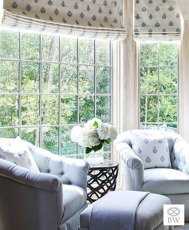 A pair of two pale blue tufted chairs and ottoman sit in front of a bedroom bay window.