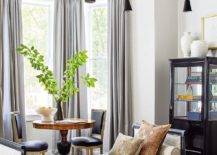 Contemporary living room designed with a black French daybed and stripe bolster pillows on a gray and tan rug in front of a bay window with black French chairs and an antique table.