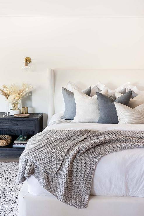 The bedroom has a white wing-back bed with dark gray pillows and a black oak nightstand lit by glass and brass sphere sconces.