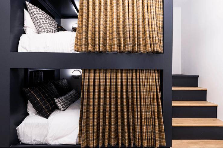 Bedroom features black bunk beds with black and white bedding, gold and brown plaid privacy curtains and a built-in staircase.