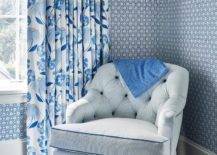 Bedroom features a blue pinstripe tufted chair with skirt, blue and white wallpaper and a blue and white curtain.