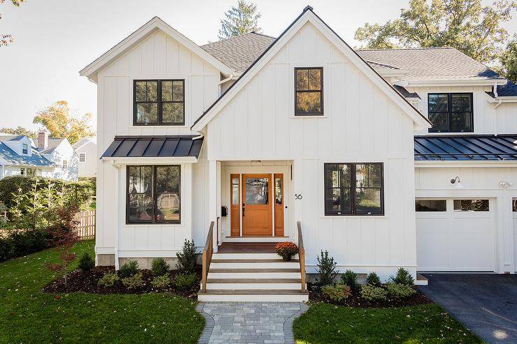 A gray brick pavers lead to a black and white craftsman style home accented with modern numbers and white board and batten siding.