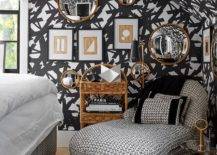 Chic contemporary bedroom is covered in black strokes print wallpaper and features a stunning black and white houndstooth chaise lounge placed on a black cowhide rug. Tan and white abstract art is hung in black frames is hung beneath and beside gold framed round convex mirrors.