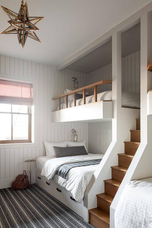 Cottage style boys' bunk room is lit by a Moravian star pendant hung over a white and gray rug. Beadboard walls are fixed behind a two tone built-in bunk bed fitted with storage drawers and a staircase.
