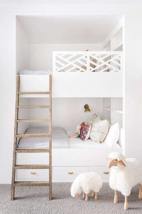 Alyssa Rosenheck - Nicole Davis Interiors reveals a kids shared bedroom with white bunk beds featuring headboard shelves that can be used as a bookshelf, storage or a place to display decor or toys. White trellis bunk bed railing and rustic wood ladders make this custom design unique with a modern twist.