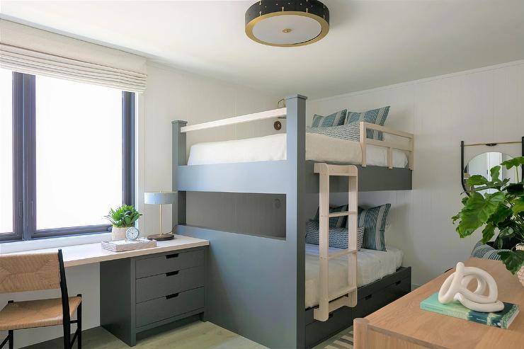 A gray built-in desk paired with an abaca chair is fixed against a blue gray bunk bed fitted with a light brown wooden mini ladder and safety railing.