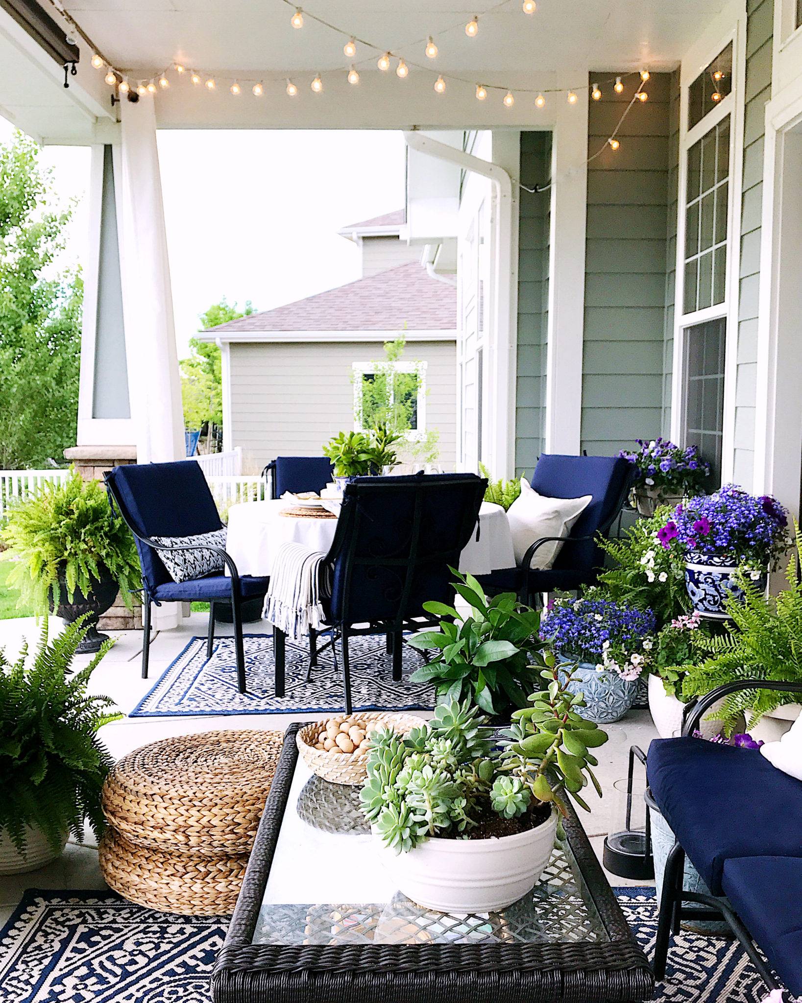 outdoor patio with fairy lights, blue velvet outdoor furniture surrounding table with white cloth, cacti accents and patterned rugs