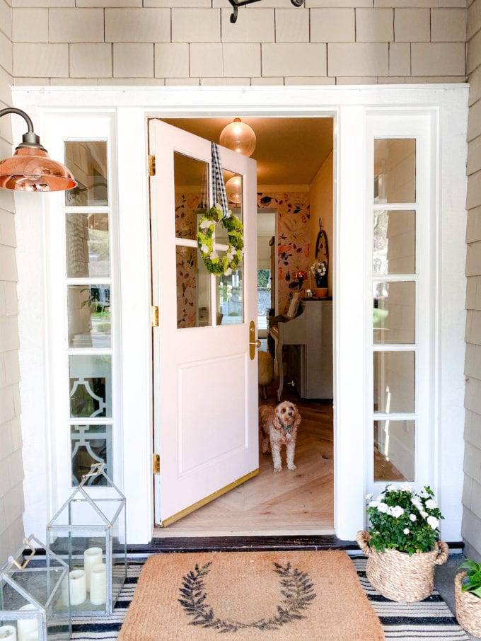 front porch with welcome mats and lanterns on ground, door open to show small dog