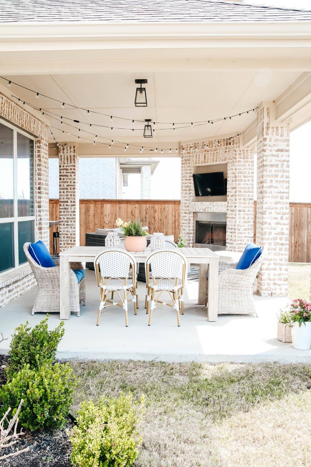 covered patio with large white table and chairs, bright pink flower pot, outdoor television and fireplace