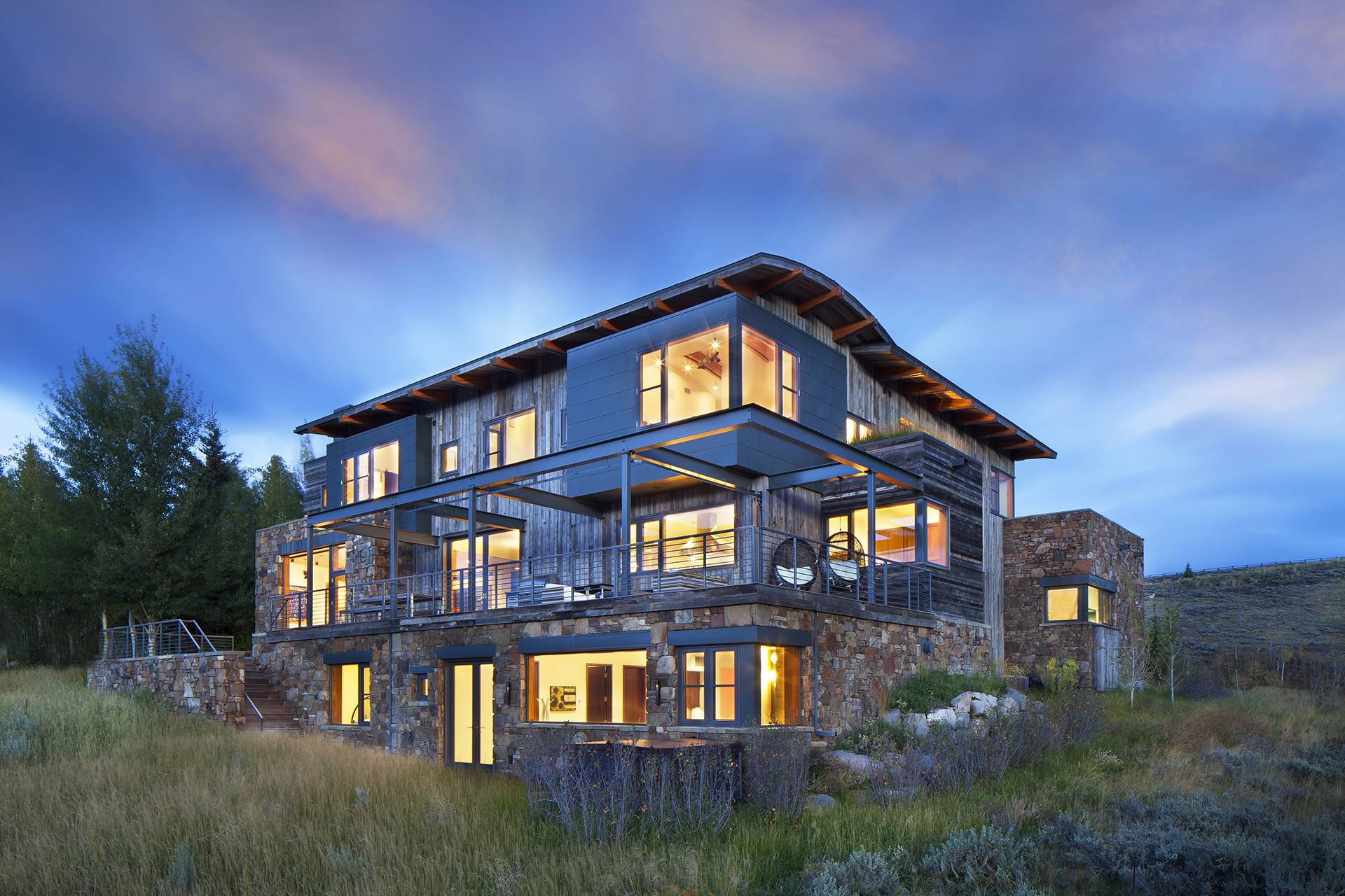 exterior of wood and stone home at sunset with lit up windows