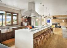 bright kitchen with large window over sink, white kitchen island with light wood stools and silver stove range hood