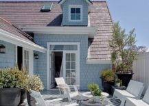 Blue shake sliding cottage cottage with gray roof features white Adirondack chairs with round gray coffee tables on blue and black geometric pavers.