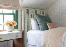 Attic bedroom features a white and brown nightstand accented with brass hardware and an an ivory and green striped headboard accented with tan and green pillows on Serena & Lily Feather Wallpaper.