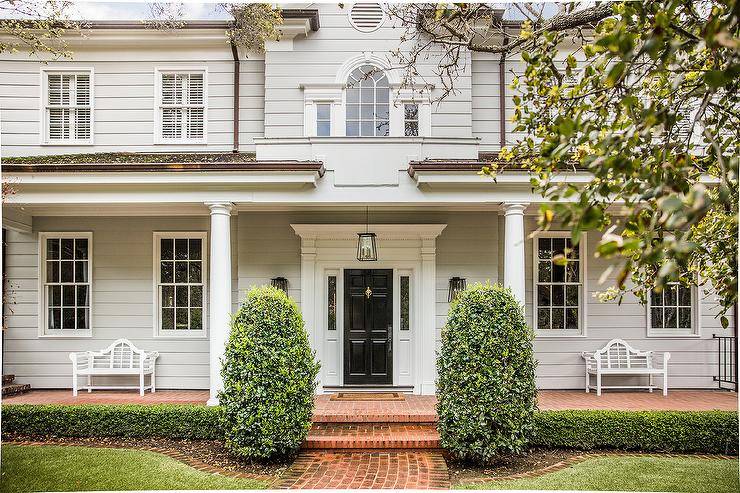 Light gray home siding featuring doric front porch column, a black front door and red brick pavers. Lush green landscape provides the perfect curb appeal to this gray two story home.