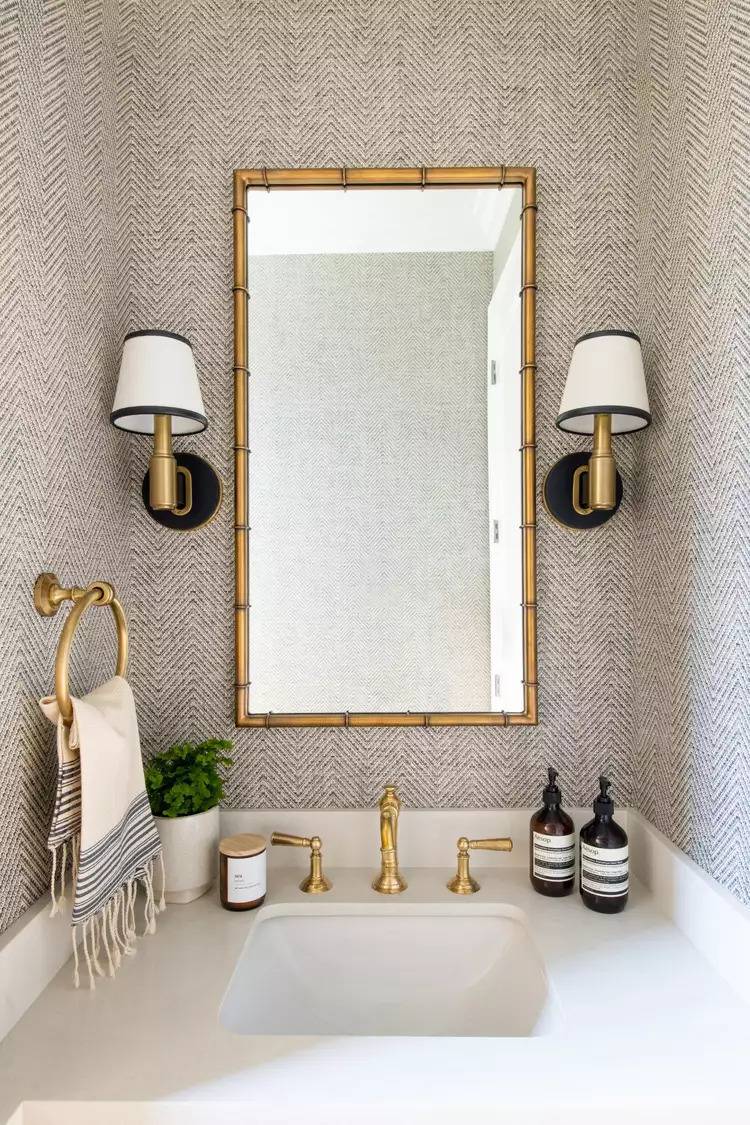beige textured wallpaper surrounding bathroom vanity with gold and black accents