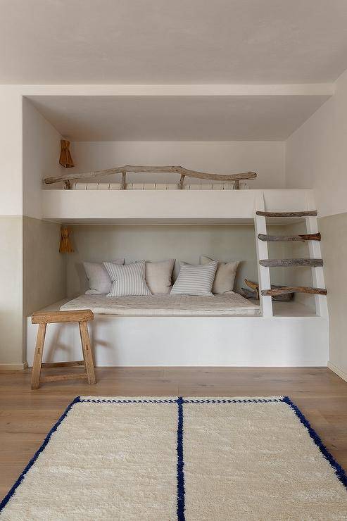 Bedroom features a built in bunk bed with branch ladder, a branch bunk bed rail, a wooden stool and a white and blue rug.