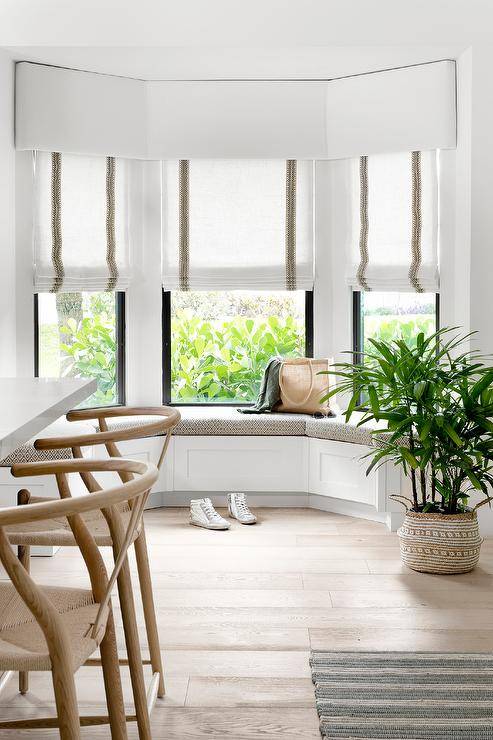 Green trimmed roman shades are layered under a white valance and hung from bay windows positioned over a built-in kitchen bench.