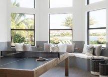 Chic game room features a bay window fitted with gray window seats alongside white and gray cushions. A modern ping pong sits in front of a bay window.