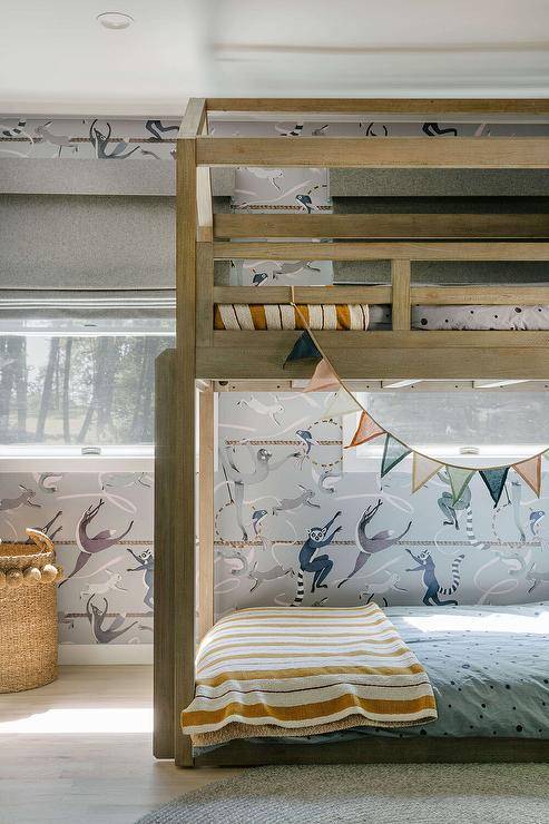 Modern boy's bedroom features a light brown house shaped bunk bed with vintage yellow striped blankets and blue Hygge & West balancing act wallpaper.