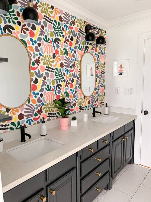 multicolored assorted shapes on bathroom wallpaper with black cabinets and gold mirror