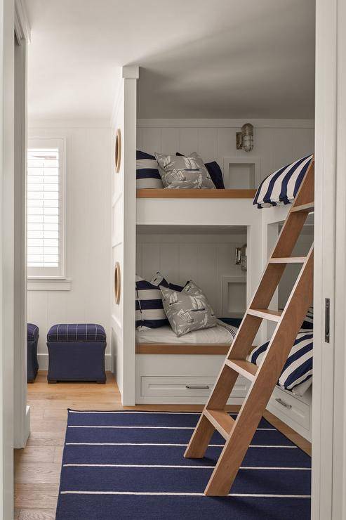 Nautical bunk room features built in bunk beds on shiplap with navy blue striped awning bedding, a navy blue striped rug and a wooden bunk bed ladder.