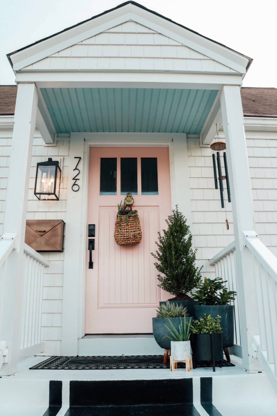pink front door with large plants on porch and hanging basket on door