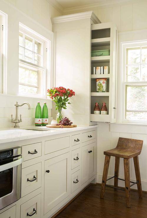 Cottage style kitchen pantry with pull out shelves and light tan shaker cabinets accented with oil rubbed bronze hardware. White quartz counters enclose an under counter microwave drawer while surrounding a vintage style satin nickel faucet.