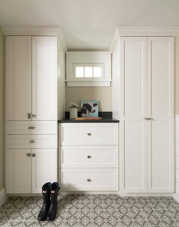 White and gray laundry room with floor to ceiling white shaker built-in cabinets accented with styled nickel knobs. A black quartz countertop centers between the cabinets above three drawers. White and gray mosaic cement tiles bring charm and style to the laundry room farmhouse design.